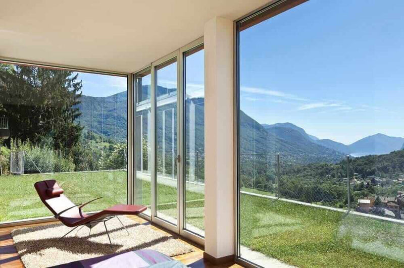 Bright living room with large windows overlooking a scenic mountain view and green lawn.