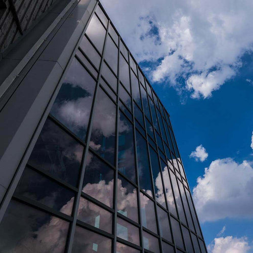 Modern building with reflective glass windows showcasing a blue sky and clouds.